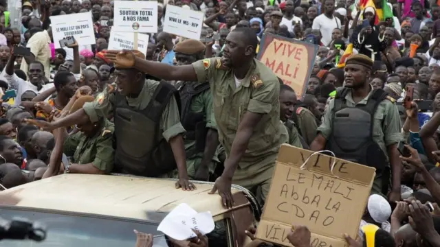 Demonstrators gather around a group of Malian soldiers during a protest to support the Malian army and the National Committee for the Salvation of the People (CNSP) at the Independence square in Bamako, on August 21, 2020, 3 days after the military overthrow of the President. - Opposition supporters flooded into Bamako's central square on August 21 to celebrate the military overthrow of the President, which their leaders hailed as the "victory of the Malian people". Thousands gathered in the capital's Independence Square, the birthplace of a months-long protest movement, many of them draped in Mali's national flag and blasting on vuvuzela horn.