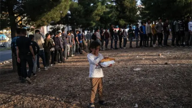Afgan bir kız çocuğu elindeki ekmekle göçmenlerin oluşturduğu kuyruğun önünde bekliyor.