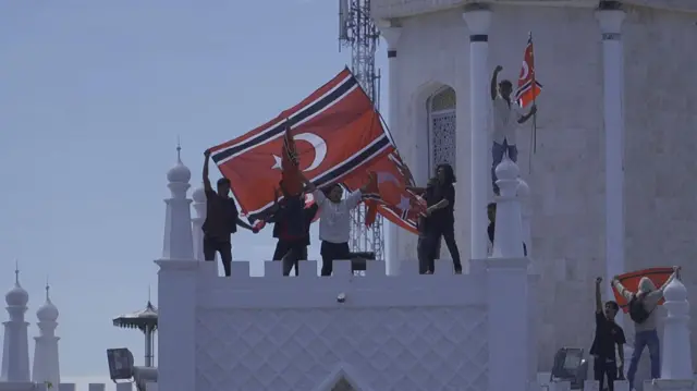 Sejumlah orang membentang bendera bulan bintang di Masjid Raya Baiturrahman, Banda Aceh, dalam Peringatan 21 tahun Hari Damai Aceh, pada Sabtu (15/08).