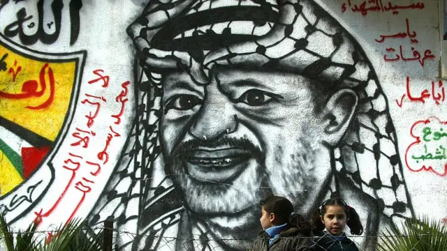 নির্বাচনের ঠিক আগে গাযা ভূখন্ডের রাফা শহরে ফাতাহ পার্টির নেতা ইয়াসের আরাফাতের প্রচারণা পোস্টারের সামনে দুজন শিশু - ২০শে জানুয়ারি ২০০৬