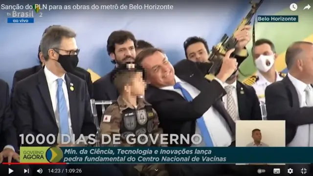 Reprodução de vídeo no Youtube mostra Bolsonaro sorrindo e apontando arma para cima, ao lado de criança e homens