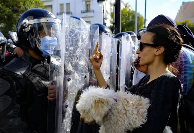 A Tunisian woman carrying a dog gestures with her middle finger as she faces police officers forming a human shield to block the access to demonstrators to the interior ministry.
