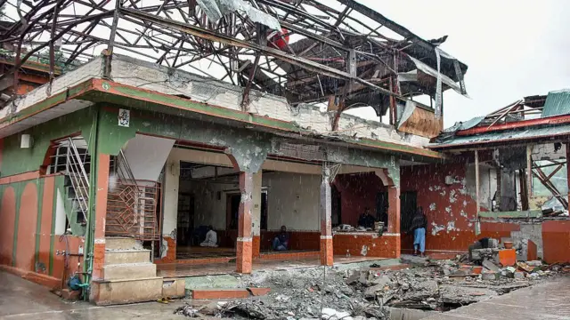 A heavily damaged mosque, its roof almost entirely torn away and its steel framework twisted and exposed against a grey sky.