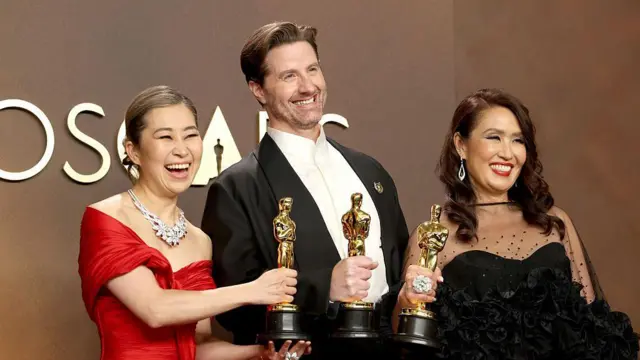 Насмејана жена у црвеној хаљини (лево), мушкарац у смокингу и жена са црвеним кармином и црној хаљини (десно) са силуетама Оскара у рукама