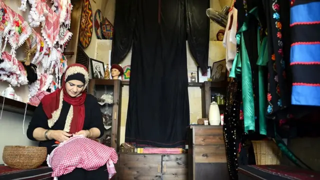 ثائرة عربيات تطرز حواف وشاحها في متجرها