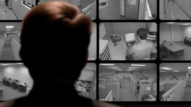 Un jefe observando a sus empleados en pantallas que captan circuito cerrado