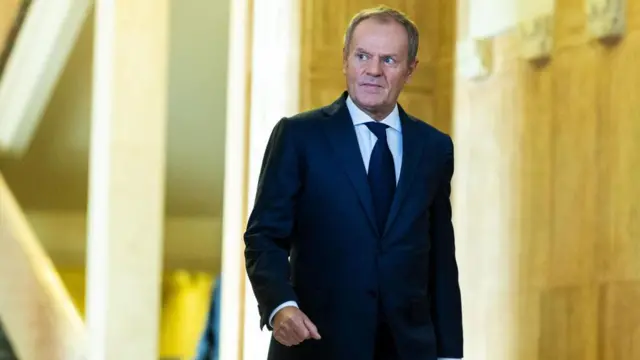 Fotosuper sorte betDonald Tusk, um homemsuper sorte betpele clara, vestindo um terno escuro sobre camisa e gravata escura. Ele está andando e olhando para o lado. 