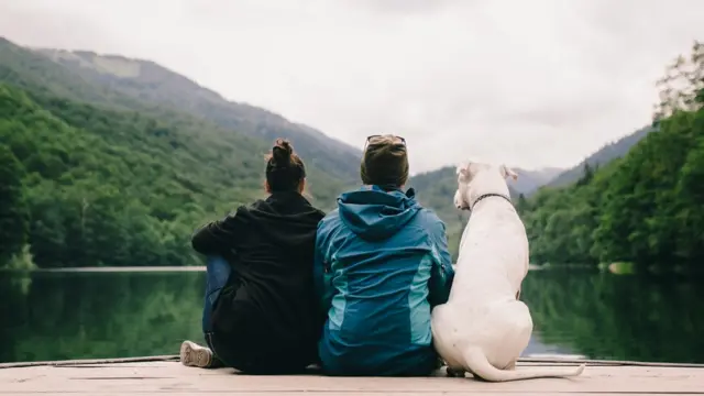 Woman, man and dog sitting on a pier, looking over a lake