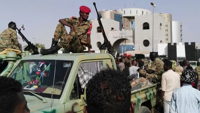 جنود سودانيون أمام مقر عسكري، حيث تجمع متظاهرون يرون أن الإطاحة بالبشير "انقلاب نفذه النظام"