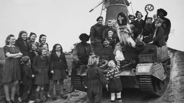 Британський солдат зображає Святого Миколая й вітає дітей, Нідерланди, грудень 1944 року.