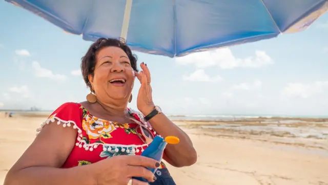 Mujer bajo sombra se aplica protector solar