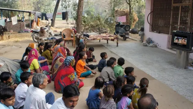 مزارعون في ولاية غوجارات يجلسون معا ويتابعون كلمات أغاني الأفلام السينمائية التي تظهر على الشاشة