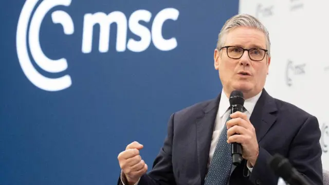 كير ستارمر يرتدي بدلة داكنة وربطة عنق زرقاء، ويحمل ميكروفوناً بيده اليسرى خلال مؤتمر ميونيخ للأمن.