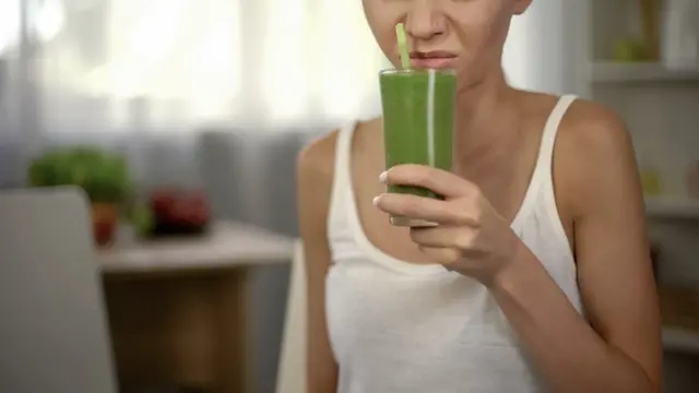 Una mujer huele con disgusto una bebida verde.