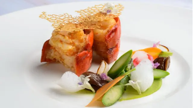 Два куска хвоста омара рядос с небольшой группой художественно порезанных овощей