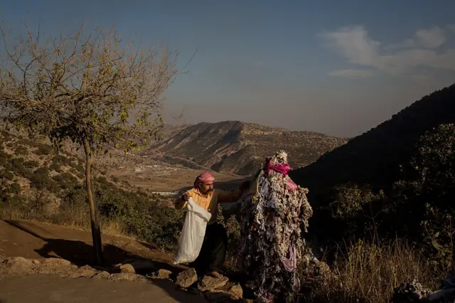 أحد خادمي الأضرحة المقدسة في لالش ينظف المكان بعد موسم الحج في عام 2016، بالقرب من مجسم تعلق عليه أقمشة للدلالة على الأماني