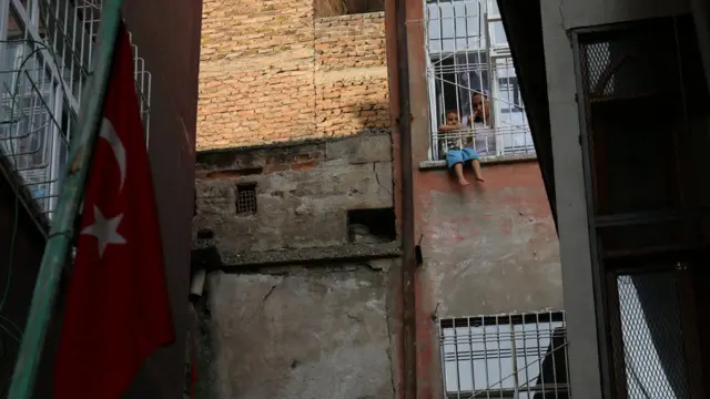 Yasağın kalktığı mahallede Türk bayrağı asılı ve bir çocuk penceren bakıyor.