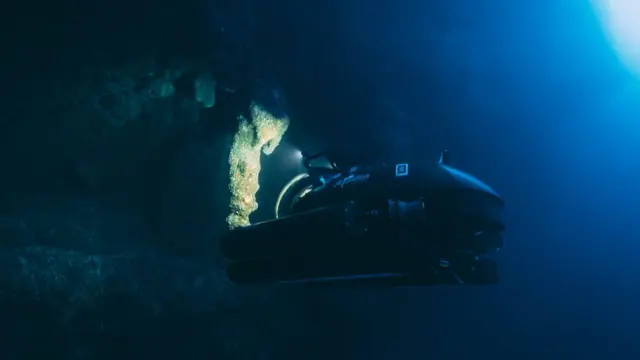 Submarino investiga as profundezas do Buraco Azulfutebol e casa de apostasBelize - imagem é toda escura, só é possível ver a luz do submarino iluminando pedaçosfutebol e casa de apostasestalactites e refletindofutebol e casa de apostasvolta no equipamento