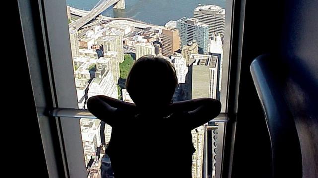 Criança olha cidade da janela de um apartamento