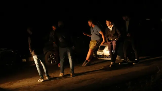 Muškarci naslonjeni na automobil razgovaraju tokom noći