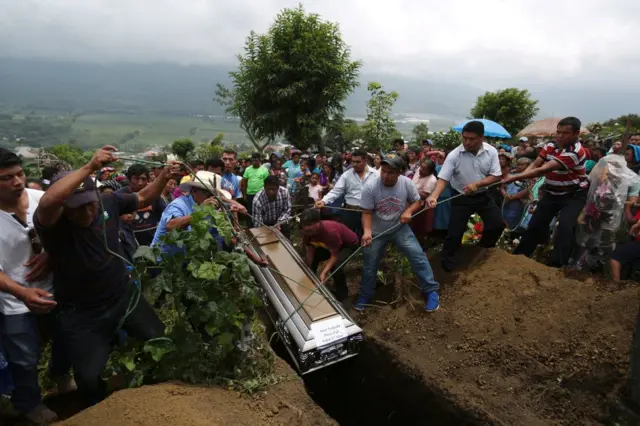 A coffin is lowered into the ground with ropes