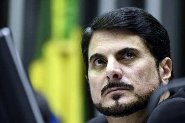 Retratoesportenet bet comclose-up do senador Marcos do Val (Podemos-ES) no plenário do Senado. Atrás, desfocada, a bandeira do Brasil. Do Val é um homem brancoesportenet bet comcabelo e barba pretas.