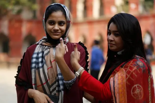 দুজন তরুণী বৃদ্ধাঙ্গুলে অমোচনীয় কালি দেখাচ্ছেন।