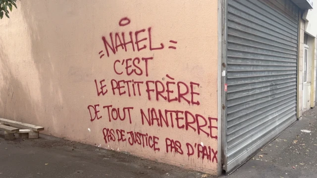 Graffiti on the side of a building in French reads "Nahel is a little brother to all of Nanterre. No justice, no peace"