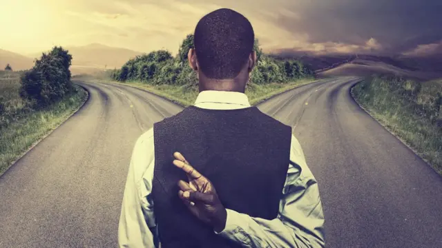 A man at a crossroads, fingers crossed behind his back.