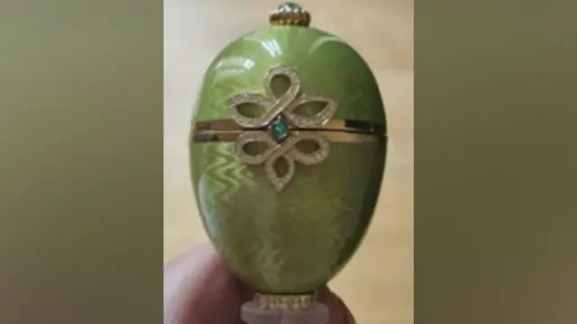 Close-up of a green Fabergé egg ornament featuring a gold band around the centre and a decorative diamond‑patterned design with a small blue‑green gemstone.
