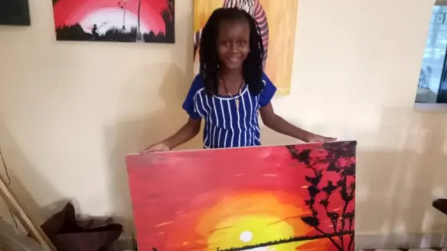 Sheila akisimama na mmojawapo wa michoro yake