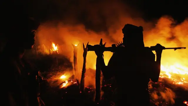 یکی از شبه‌نظامیان عرب در جنگ دارفور در کنار روستایی که به آتش کشیده شده (سال ۲۰۰۴)