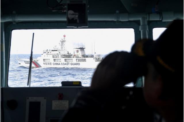 印尼军舰上士兵用望远镜查看不远处的中国海警船只。