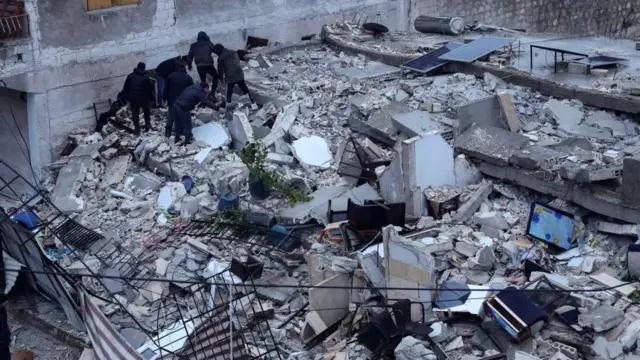 سكان يبحثون عن ضحايا وناجين وسط أنقاض مبنى انهار في قرية عزمارين، بالقرب من الحدود التركية شمالي محافظة إدلب السورية