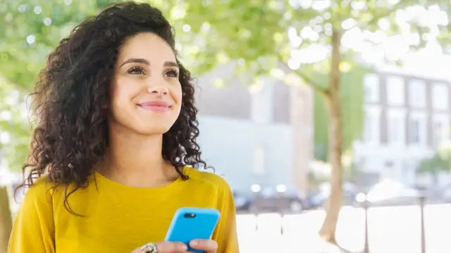 Une femme, téléphone en main, regarde vers l'horizon