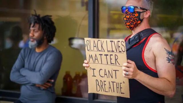 Un hombre blanco sosteniendo un cartel que dice "Las vidas negras importan. No puedo respirar".