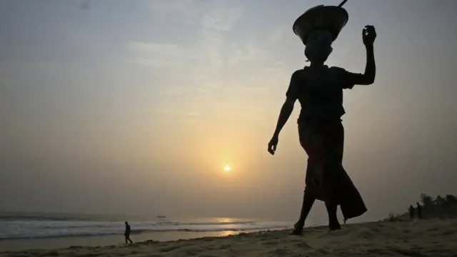 A woman walks along a beach at sunset in Grand Bassam, Ivory Coast, 27 January 2018