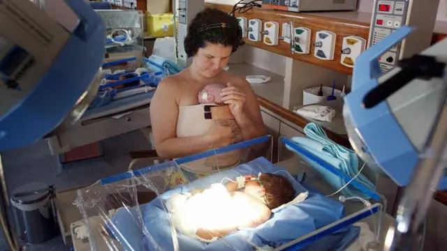 Une femme regarde un bébé dans une couveuse.