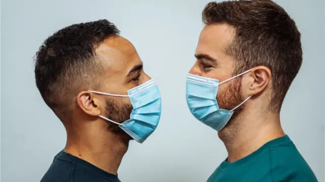 Two men wearing face masks stare at each other