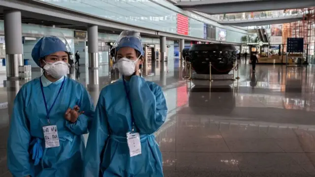 Security workers wearing protective gear as a preventive measure against the COVID-19 coronavirus walk through a nearly empty arrivals area at Beijing Capital Airport in Beijing on March 16, 2020