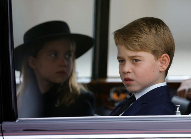 Fotografia mostra o príncipe George e a princesa Charlotte, duas crianças brancas loiras, com roupas pretas, dentro de um carro