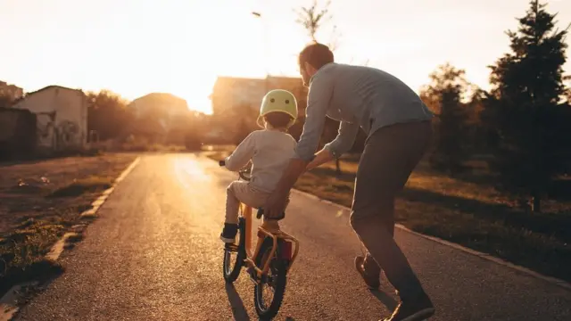 Photo of a young boy and his father on a bicycle lane, learning to ride a bike.