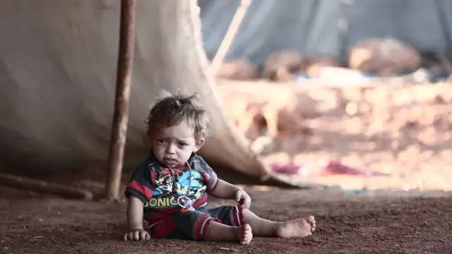 A child sits in front of a tent at a camp for displaced people in al-Ghadfa, Idlib province, Syria (2 September 2018)
