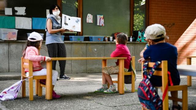 A teacher reads a book to kindergarten children in a school garden. Municipality of Ivrea opens the gardens of two kindergarten schools as part of a pilot test to see how schools can reopen after COVID-19 coronavirus lockdown.