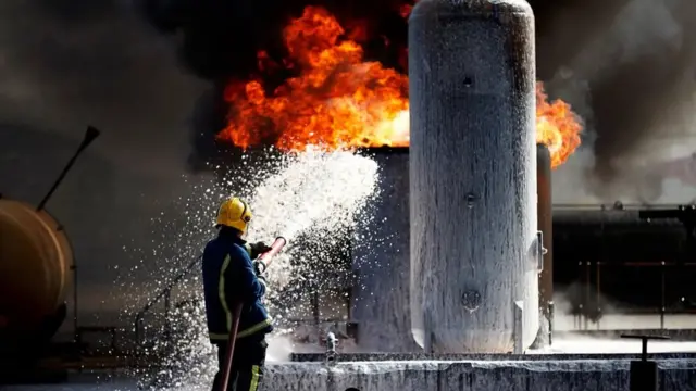 Fotografia colorida mostra bombeiro usando mangueira para apagar fogosite pixbet gratisum imóvel que parece ser industrial