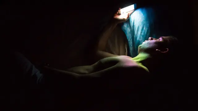 Hombre mirando un celular de noche en la cama.