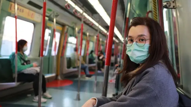 Jovem mulheraposta online esportemáscara sentada no metro olha para a camera