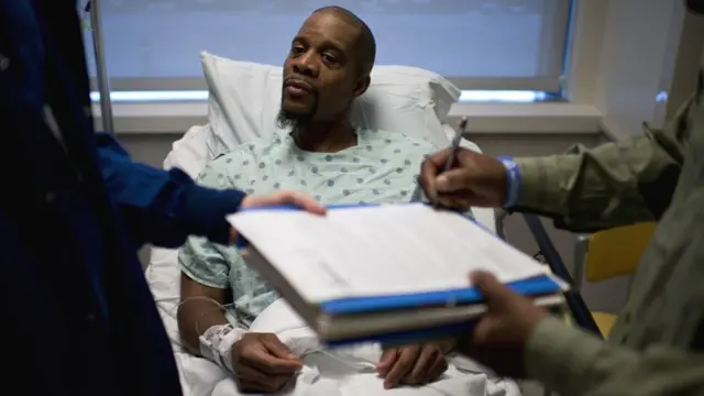 Un donante negro espera en una camilla que firmen una documentación antes de operarlo.