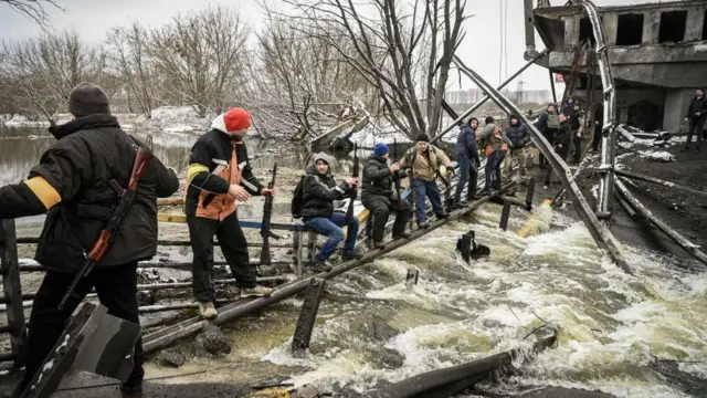 Des membres de la défense civile traversant une rivière dont le pont a sauté.