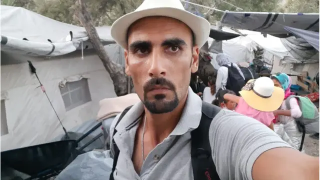 صورة لـ طالبشاه حسيني يقف إلى جوار خيمته الجديدة بمخيم موريا قبل أن تلتهمه النيران